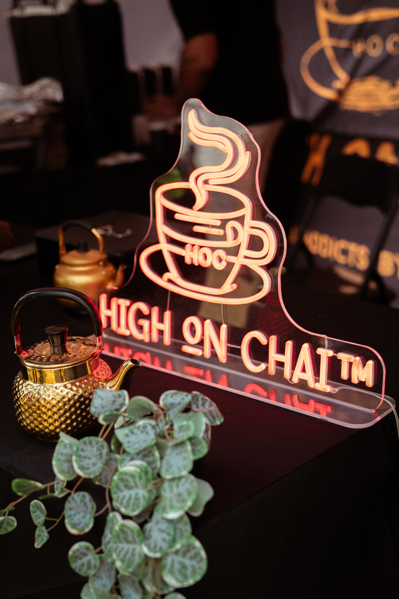 Neon sign with a coffee cup design and 'High on Chai' text, surrounded by decorative elements.