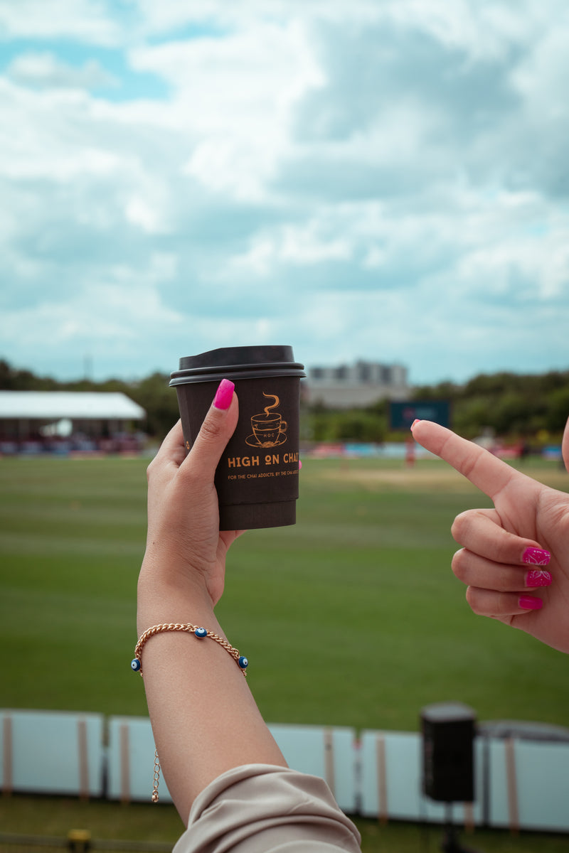 Person holding a chai cup with a blurred sports field and stadium in the background
