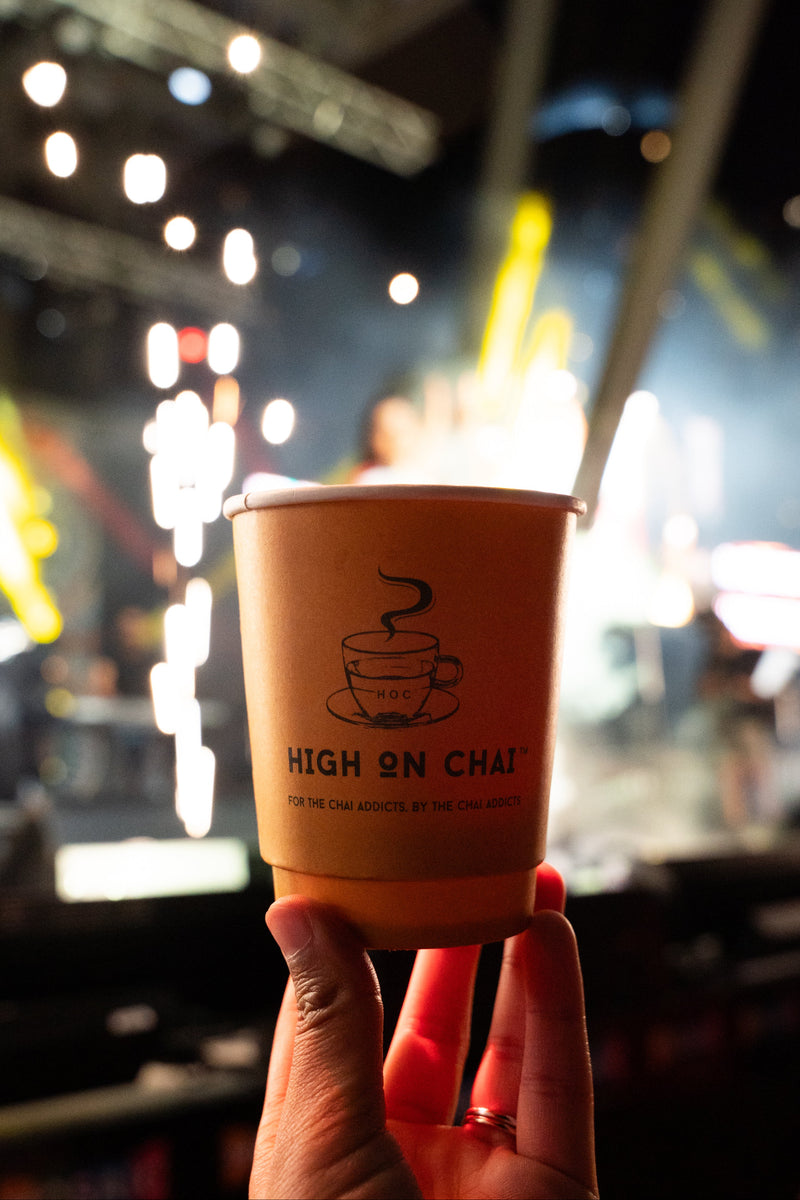 Hand holding a 'High on Chai' cup with a blurred indoor background