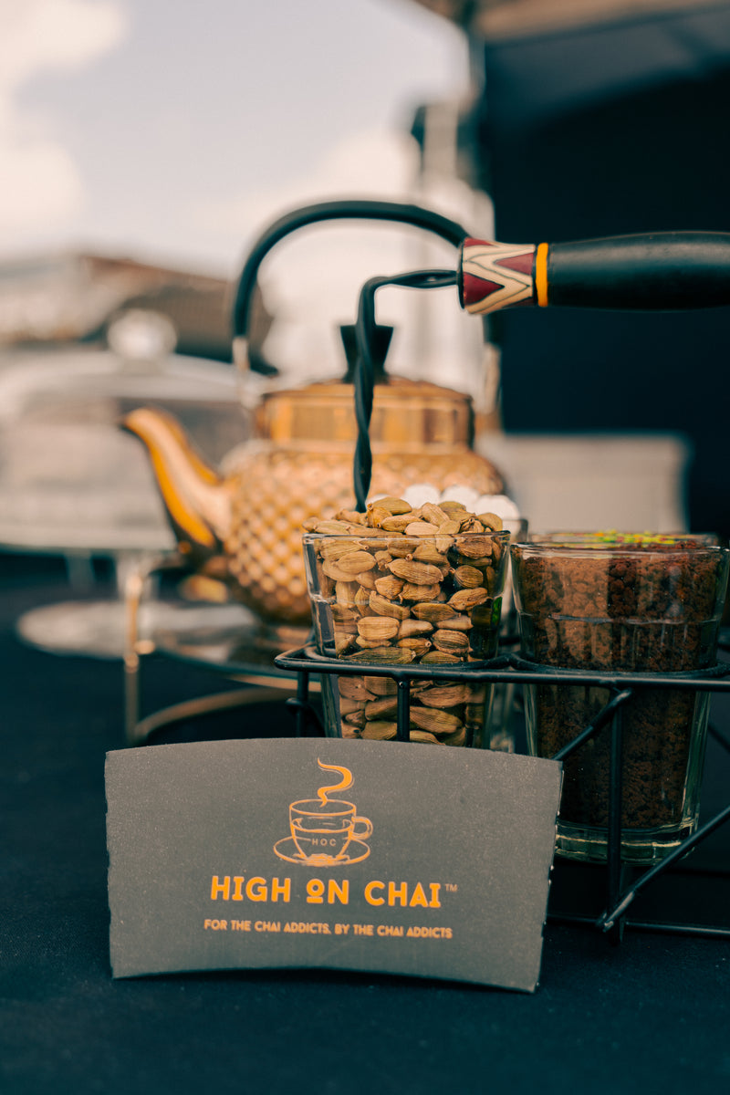 Tea-making setup with teapots and a 'High on Chai' towel in the foreground.