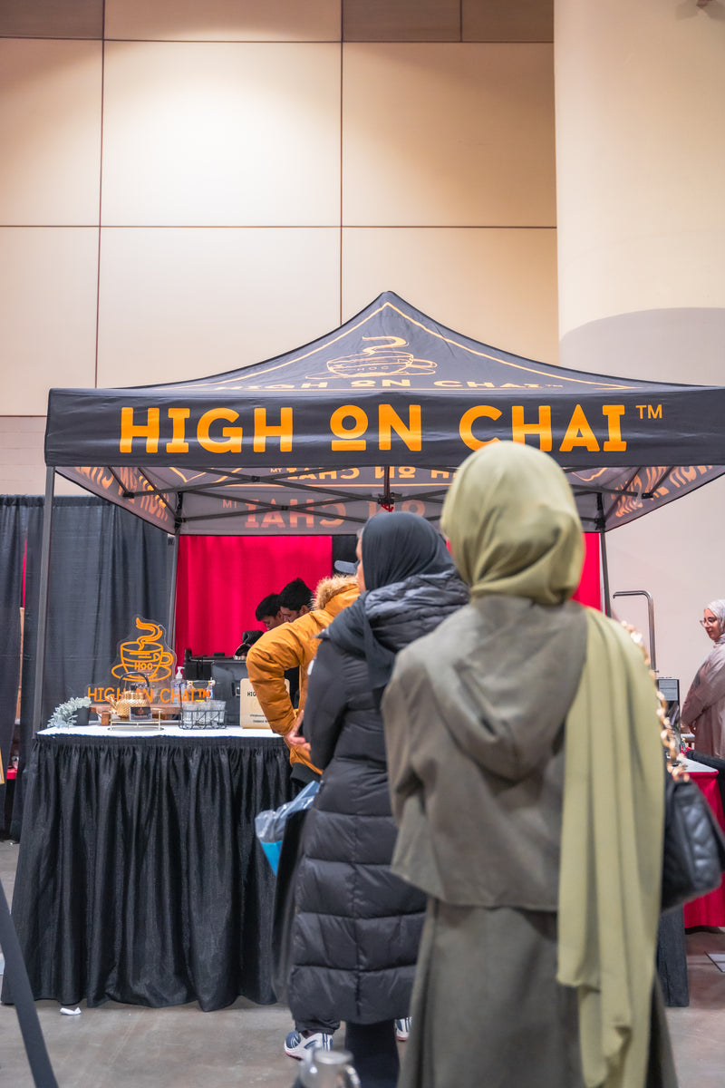 People standing in front of a 'High on Chai' booth at an event.