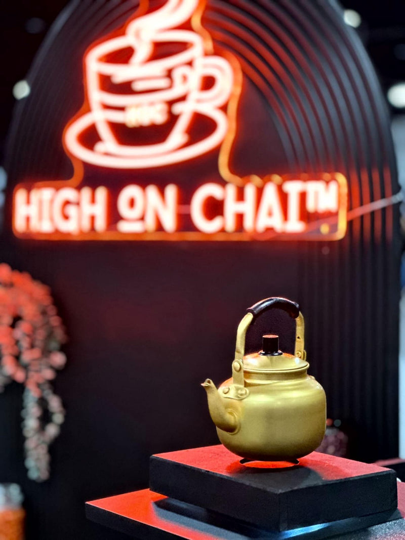 Neon sign with 'High on Chai' and a gold teapot on a black stand.