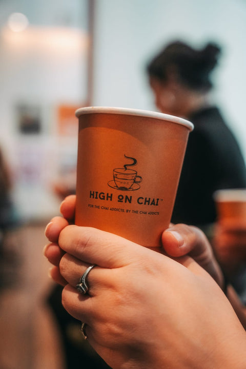 Hand holding a 'High on Chai' cup with a blurred background